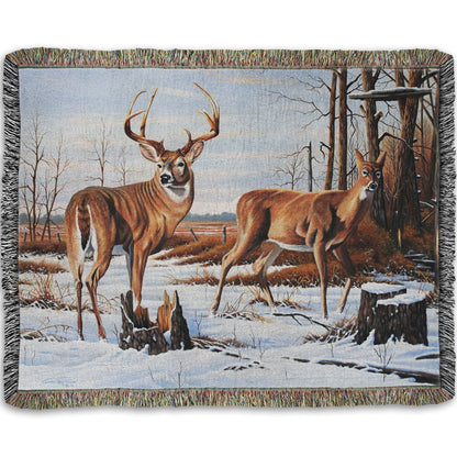 Woven throw blanket designed with deer walking through the snow between the woods and a field.
