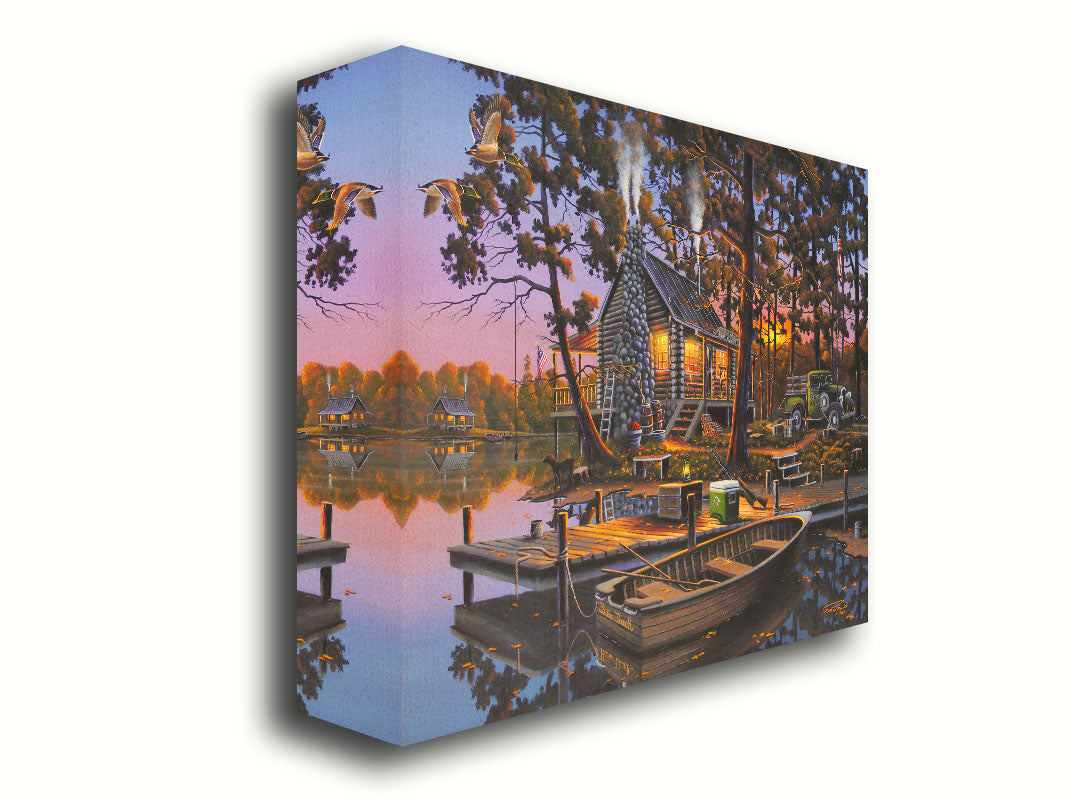 A painting of a lakeside log cabin hunting lodge at sunset. A rowboat is tied to the nearby dock, where shotguns are leaned against a cooler. Printed on canvas.