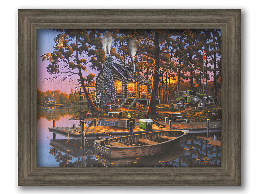 A painting of a lakeside log cabin hunting lodge at sunset. A rowboat is tied to the nearby dock, where shotguns are leaned against a cooler. Printed on canvas and framed.