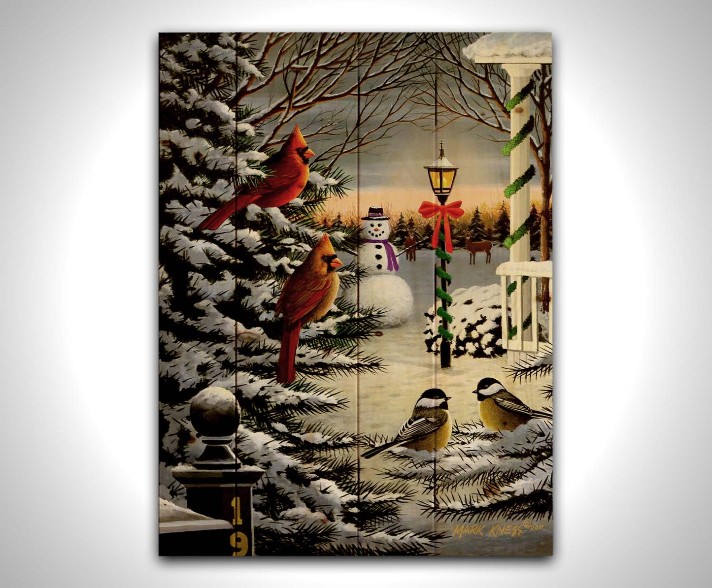 A painting of cardinals and chickadees perched on snowy evergreen branches. In the background, a festively decorated streetlamp illuminates a nearby snowman. Deer look on in the distance. Printed on a wood pallet.