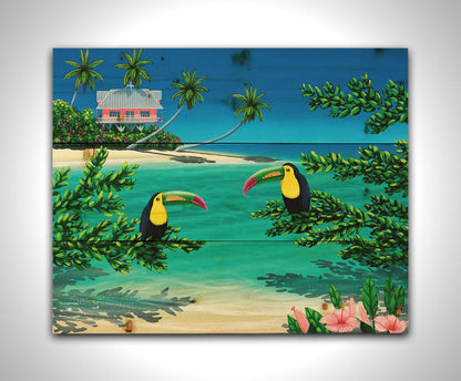 A vibrant painting of an island beach scene, featuring two toucans perched on plants in the foreground, and a bright house on stilt foundations in the background. Printed on a wood pallet.