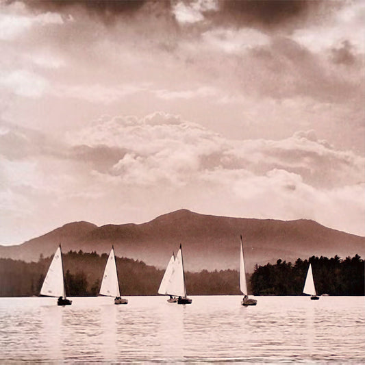 A monochrome photograph of six sailboats racing on the water with a mountain in the distance.