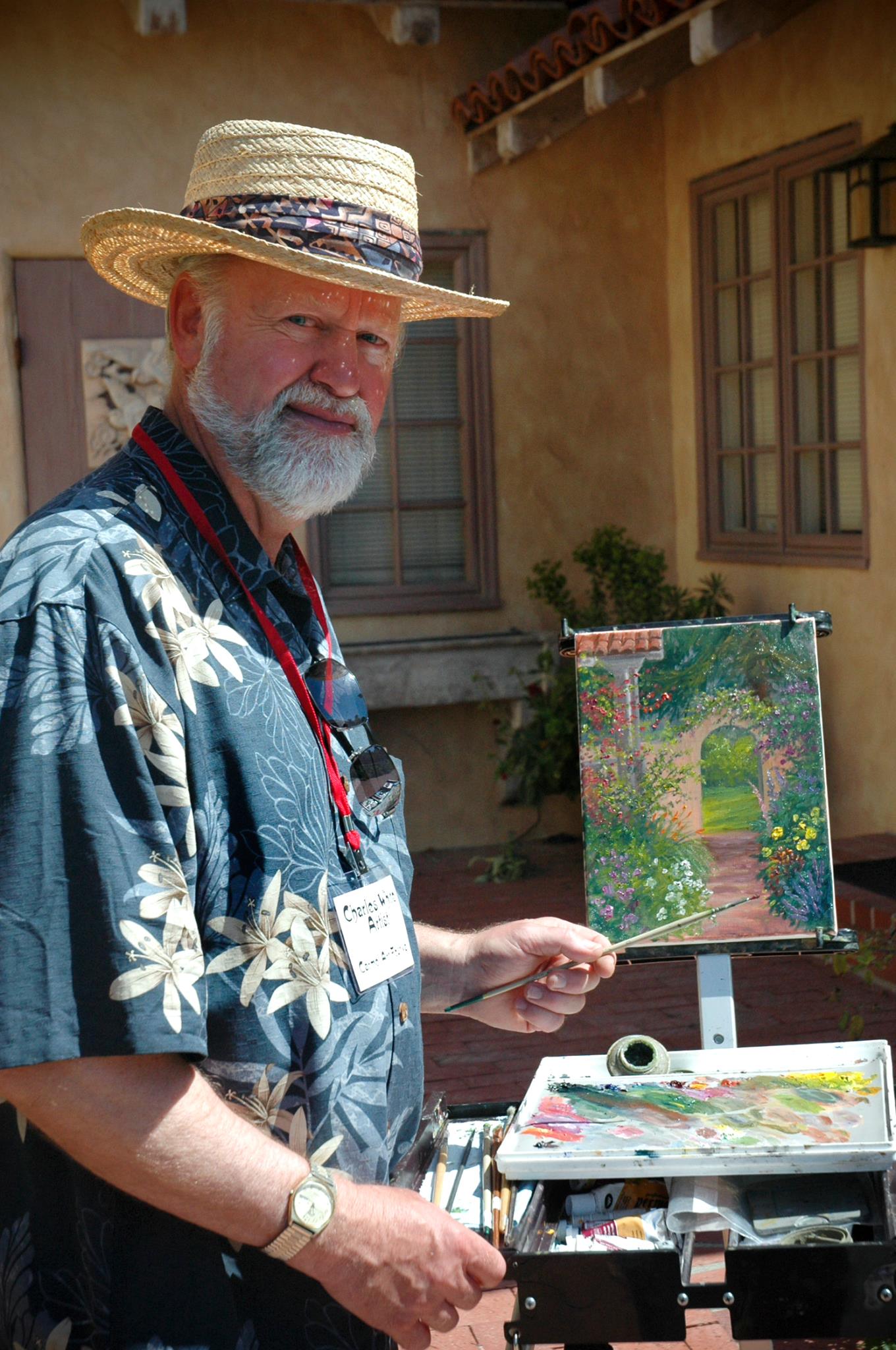 Artist Charles White standing beside a painting he is working on of an archway covered in greenery.