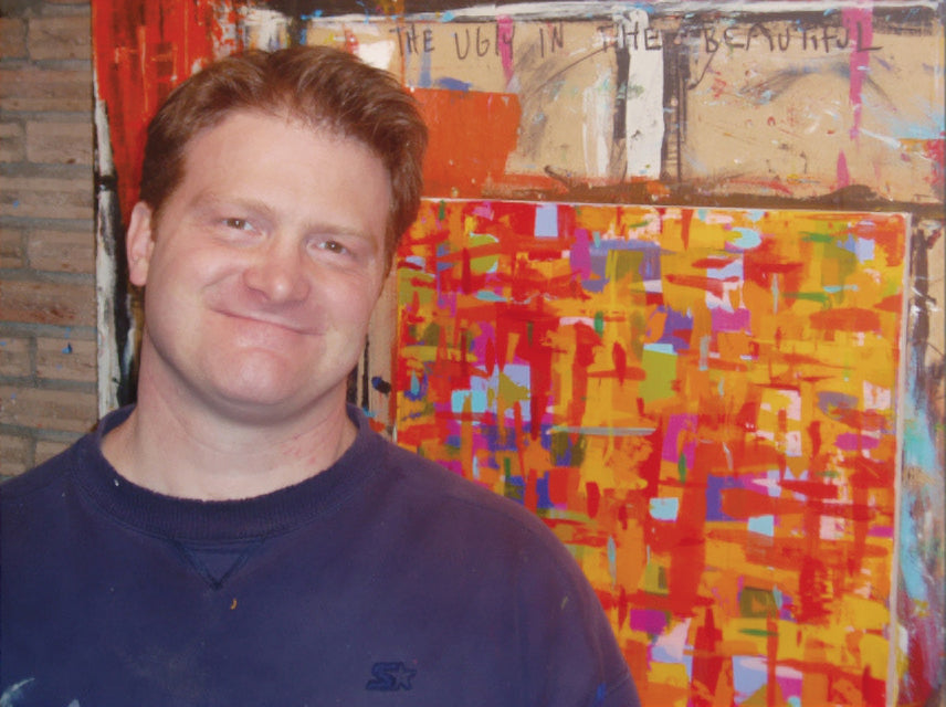 A headshot of artist Jeff Boutin. He stands in front of one of his abstract paintings.