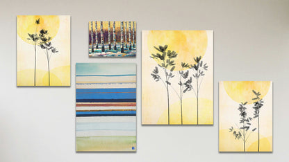 A collage of art in the standard Feeling Love package, including a series of three canvas photos of plants silhouetted against yellow skies, a canvas abstract geometric painting invoking boats and the shore, and a box board painting of birch trees in winter against a yellow sky.