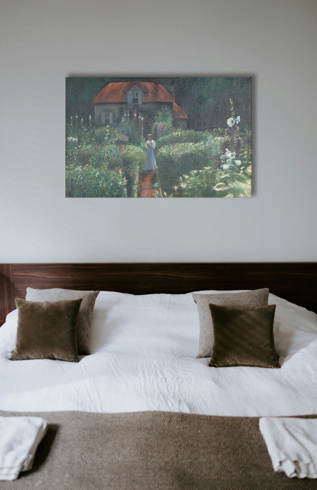 A typical bedroom with light walls and a cozy brown bed. A canvas painting of a cottage surrounded by a garden hangs on the wall.