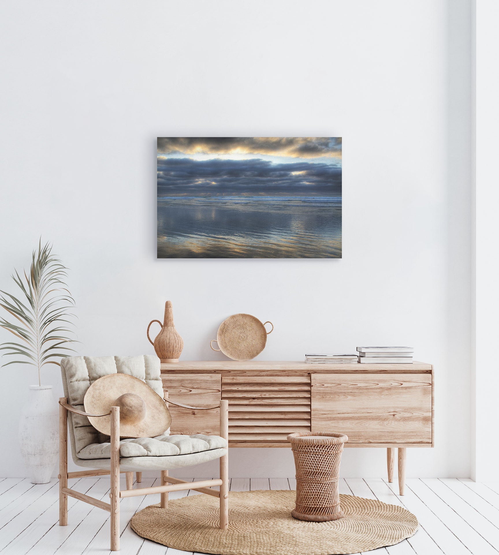 A tropical sea themed room with palm plants and light wood furniture. A canvas photograph of Scripps Pier, La Jolla, California hangs on the wall.