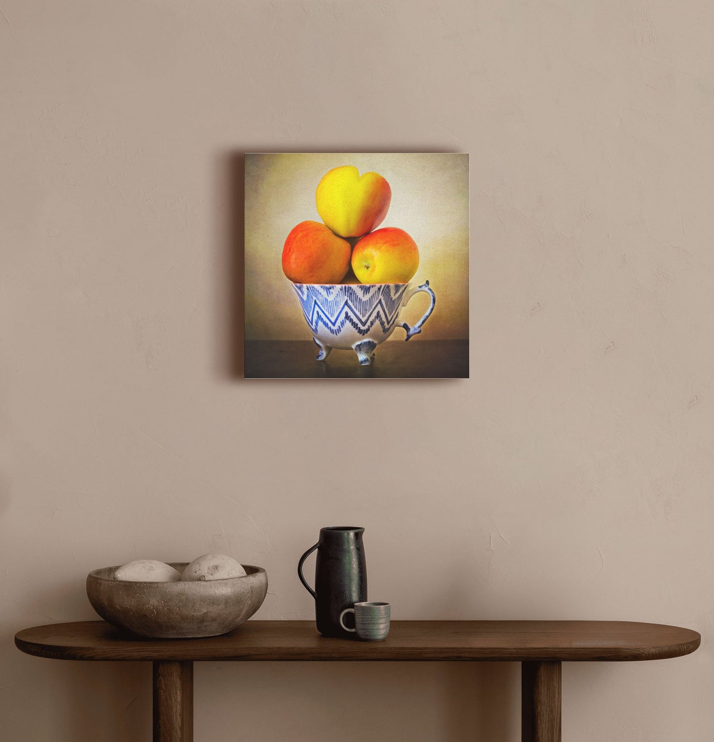 A warm hallway with a small wooden table, with a decorative bowl and ceramics. A canvas photograph of apples stacked in a cup hangs on the wall.