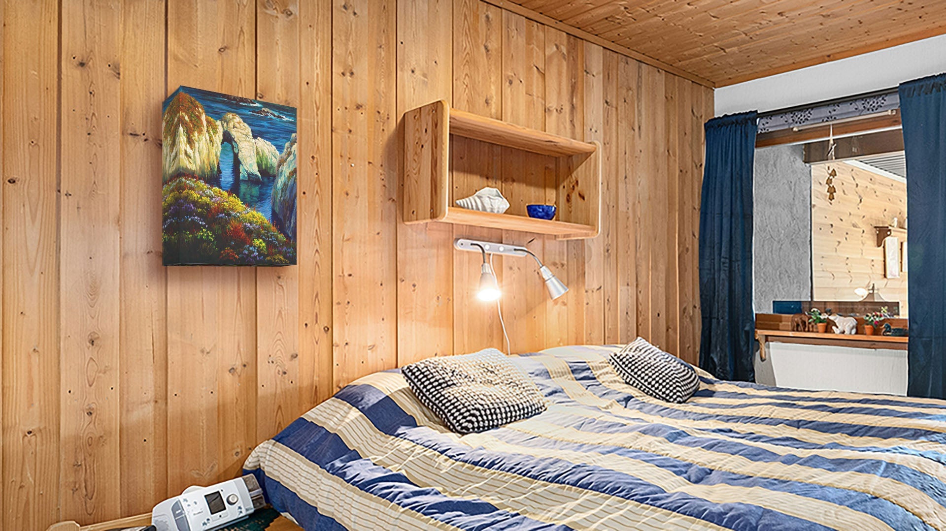 A seaside bedroom with light wood walls and blue and white furniture. A canvas painting of Point Lobos, Carmel-by-the-Sea, California, hangs on the wall.