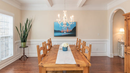 A light dining room with wood furniture, plants, and a clear chandelier. A canvas photograph from Baker Beach, looking out at the Golden Gate Bridge at night.