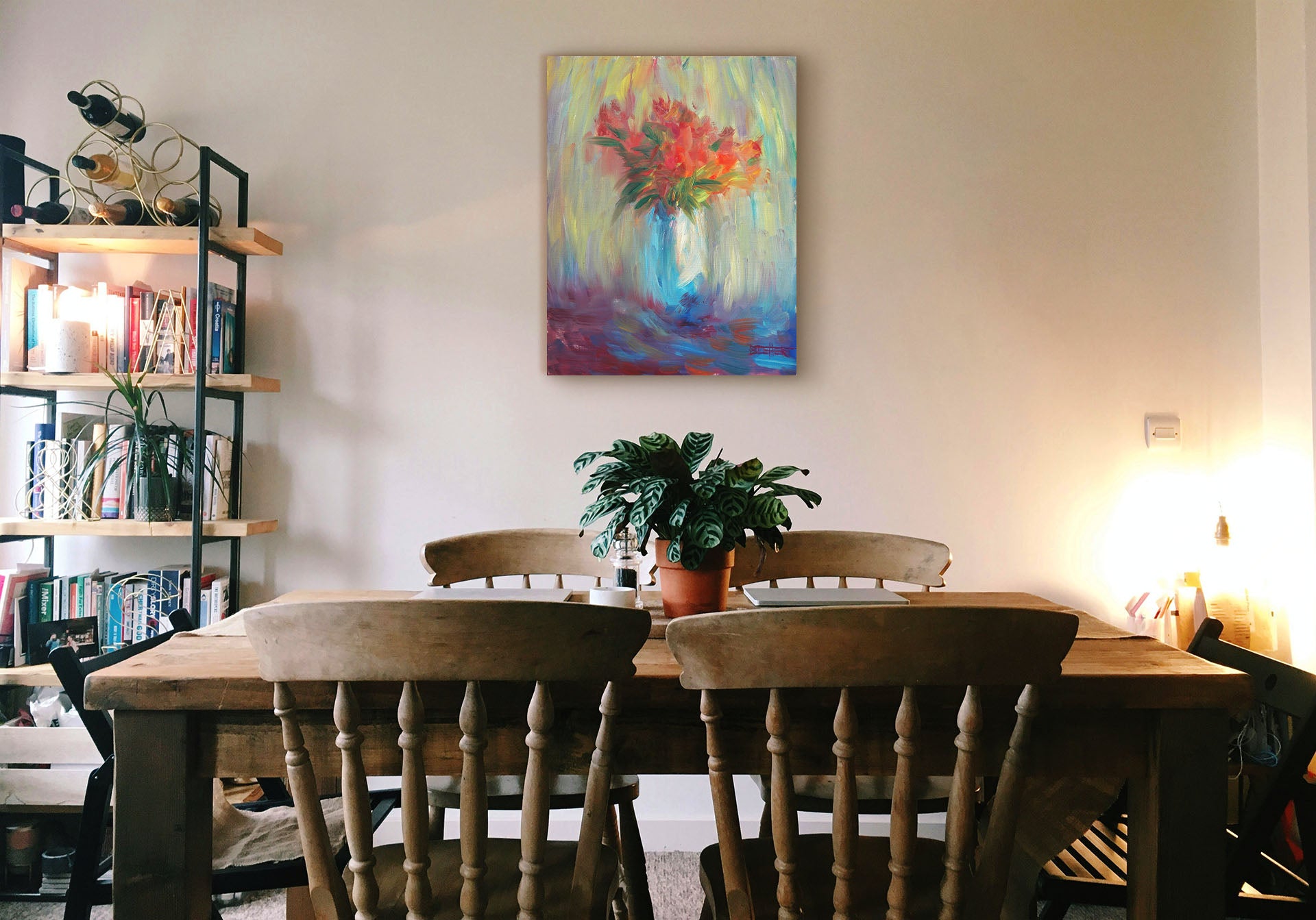 A painting hanging on a dining room wall. A still life painting of a vase of bright red flowers, created with expressive visible brushstrokes and broken color. Printed on canvas.