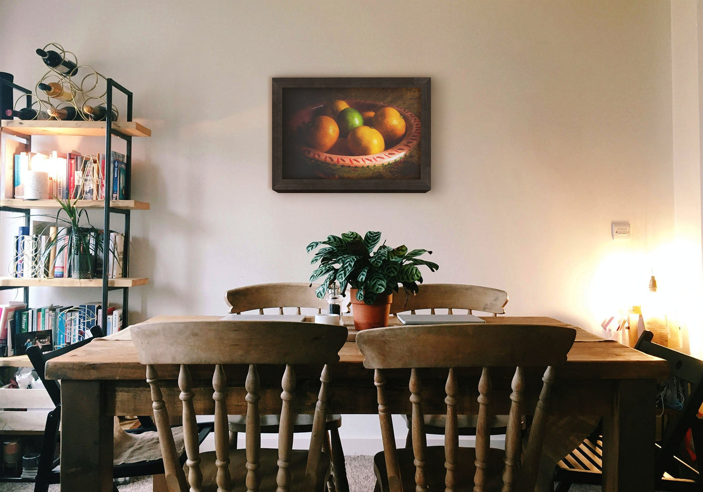 A cozy kitchen with solid wood furniture and gentle lighting. A framed photograph of a bowl of fruit hangs on the wall.