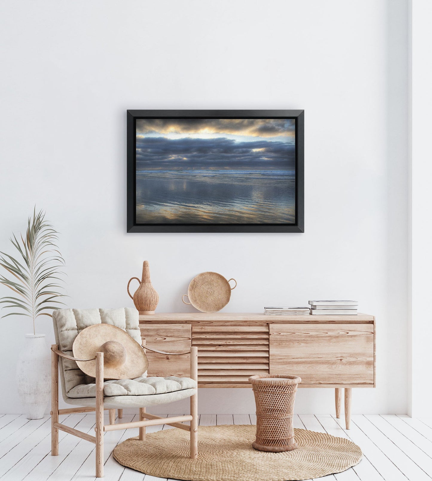 A tropical sea themed room with palm plants and light wood furniture. A framed photograph of Scripps Pier, La Jolla, California hangs on the wall.