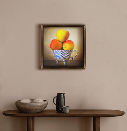 A warm hallway with a small wooden table, with a decorative bowl and ceramics. A framed photograph of apples stacked in a cup hangs on the wall.