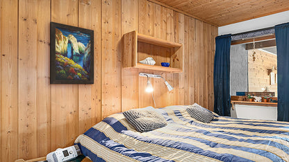 A seaside bedroom with light wood walls and blue and white furniture. A framed painting of Point Lobos, Carmel-by-the-Sea, California, hangs on the wall.