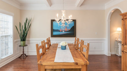 A light dining room with wood furniture, plants, and a clear chandelier. A framed photograph from Baker Beach, looking out at the Golden Gate Bridge at night.