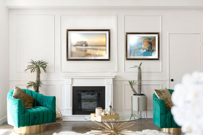 A tropical sea themed living room with highly designed white walls and teal furniture. Two matted and framed artworks hang on the wall– a photograph of Natural Bridges in Santa Cruz, California, and a painting of the view from Rocky Point at Big Sur, CA.