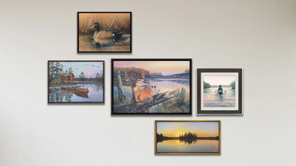 A collage of art in the luxury By Dawn's Early Light package, including a float framed painting of a deer standing in a lake at sunrise, a float framed painting of a blue-winged teal swimming in a brown scene, a float framed painting of a lakeside cabin and docked rowboat, a float framed painting of a calm lake reflecting the low sun, and a matted and framed painting of people paddling a canoe across a lake on a peaceful, misty morning.