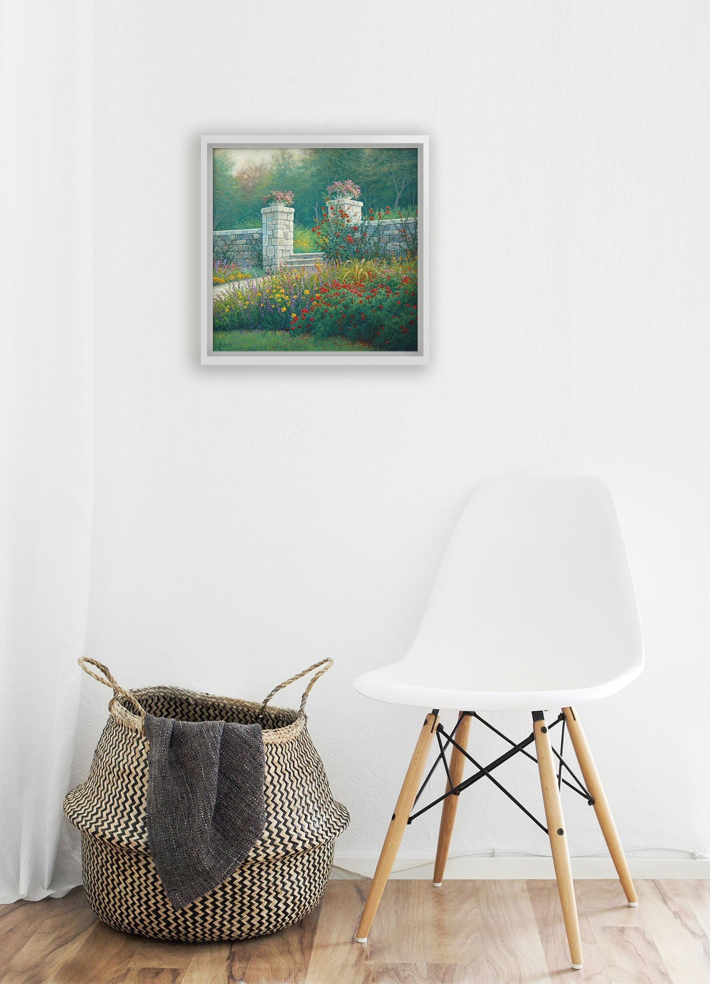 A white room with wood accents and a woven basket. A float framed painting of a walled garden hangs on the wall.