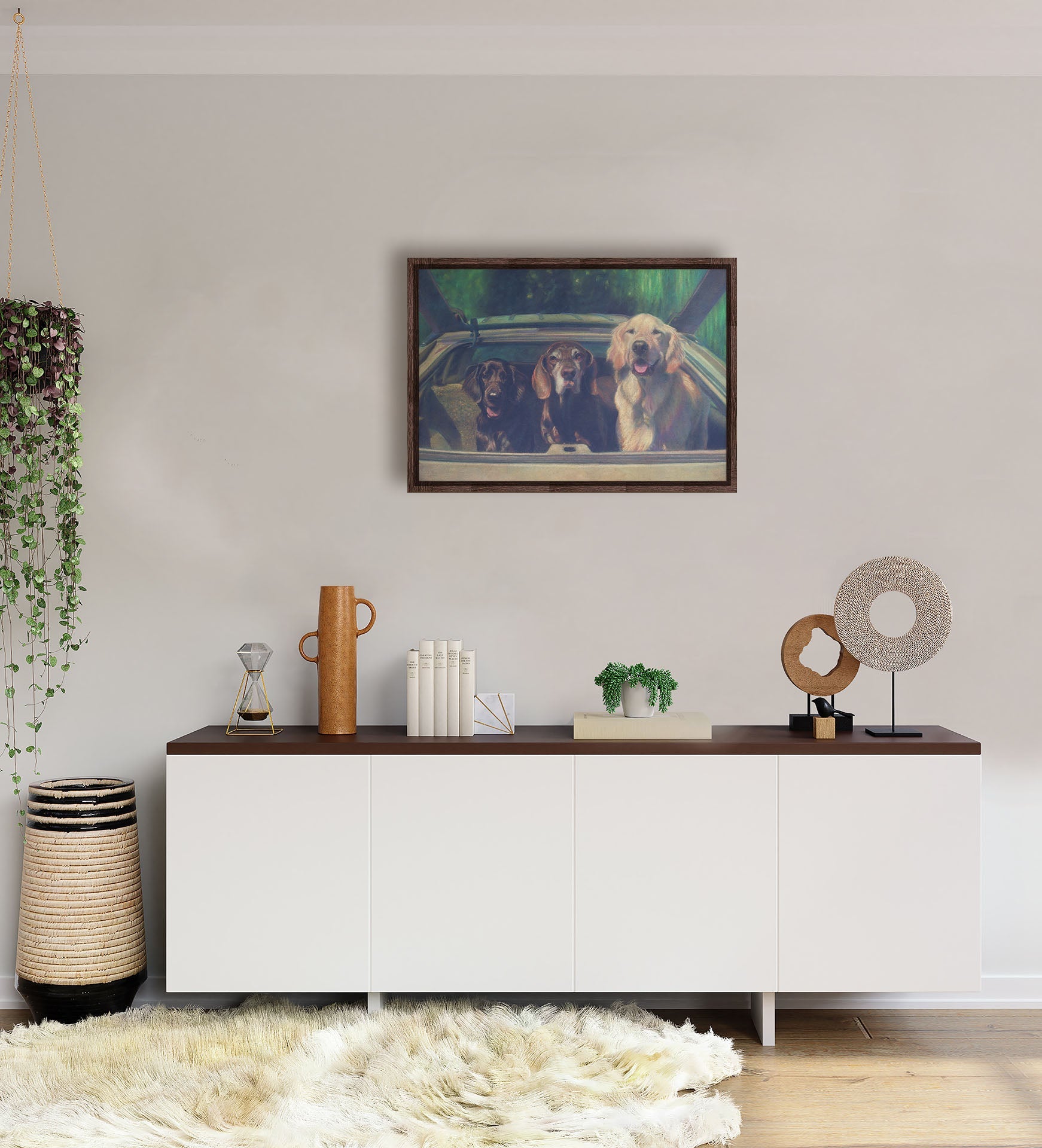 A white-walled room with a long, white cabinet decorated with sculptures, plants, and a woven basket. A float framed painting of three dogs riding in a car hangs on the wall.