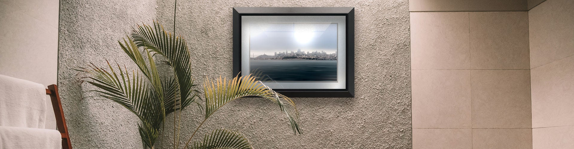 A tropical sea themed bathroom with palm plants and a large tub. A matted and framed photograph overlooking the coast of San Francisco hangs on the wall.