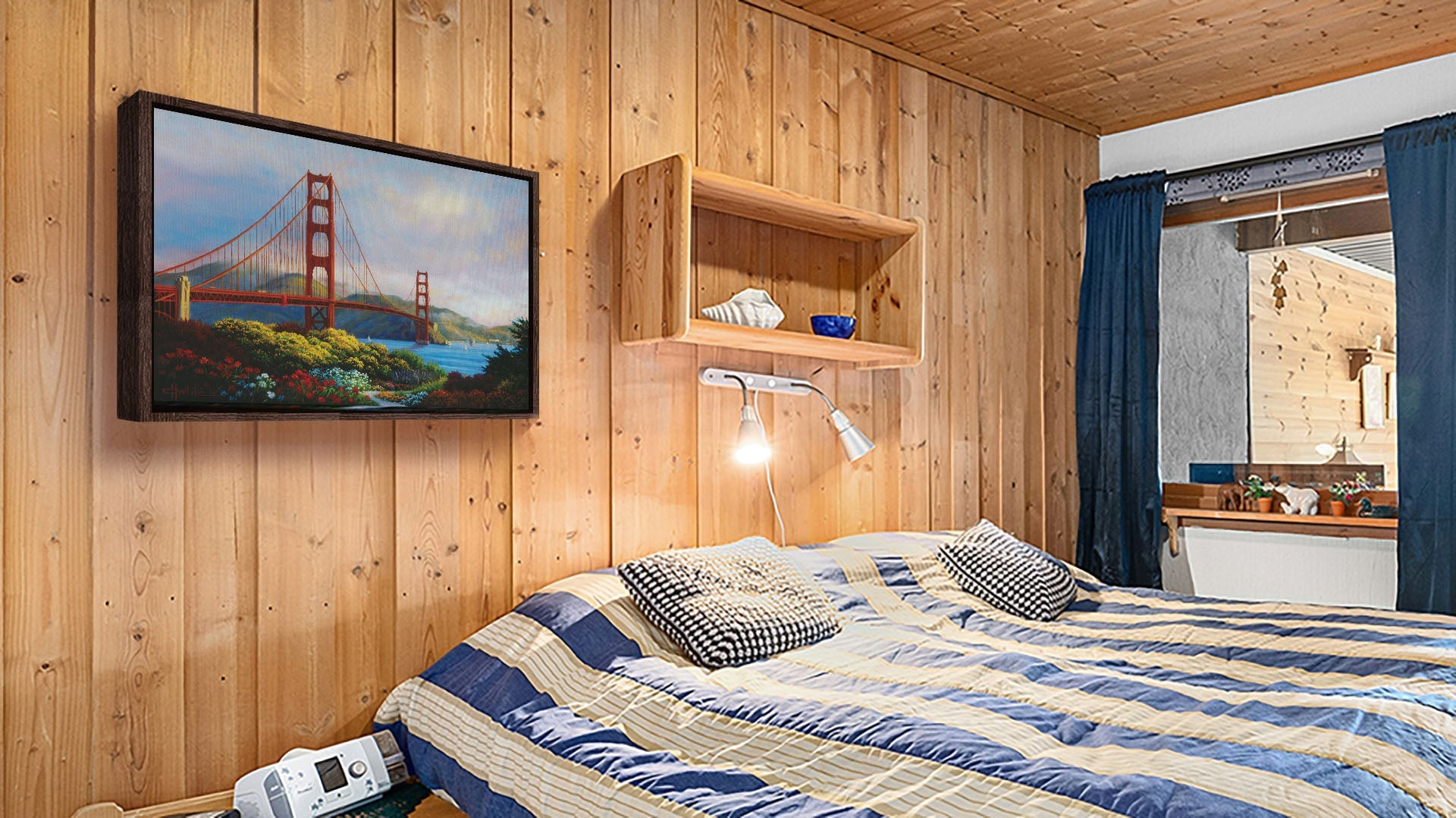 A seaside bedroom with light wood walls and blue and white furniture. A float framed painting of the Golden Gate Bridge in San Francisco, California, hangs on the wall.