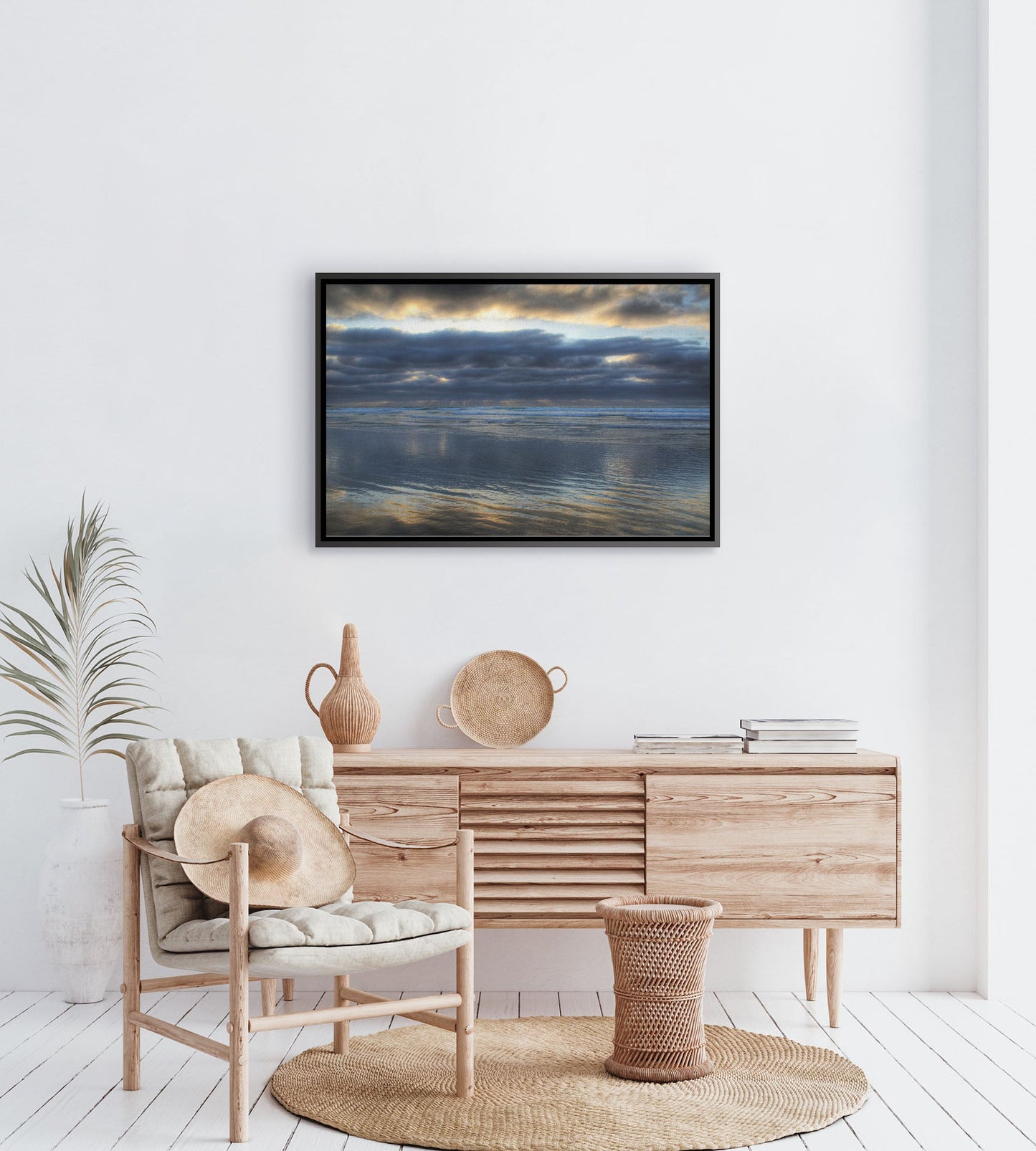 A tropical sea themed room with palm plants and light wood furniture. A float framed photograph of Scripps Pier, La Jolla, California hangs on the wall.