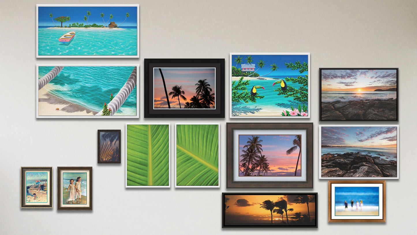 A collage of art in the luxury Pastel Palms package, including two matted and framed paintings of kids on the beach; two matted and framed photos of palm trees; a matted and framed photo of kids on the beach; a framed photo of tropical plants at sunset; three float framed paintings of an island beach, a rowboat at an island, and toucans perched on beach plants; two float framed photos of Manly Beach, Australia; two float framed photos of bird of paradise palms; and a float framed photo of a sunset in Maui.