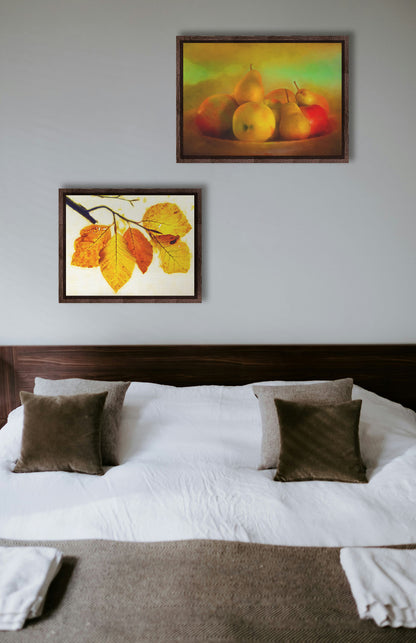 Two paintings hanging on a bedroom wall. The first is a photo of a dish of apples and pears, in a greenish yellow light. Printed on canvas in a float frame. The second is a photo of a twig of orange and yellow leaves on a white background. Printed on canvas in a float frame.