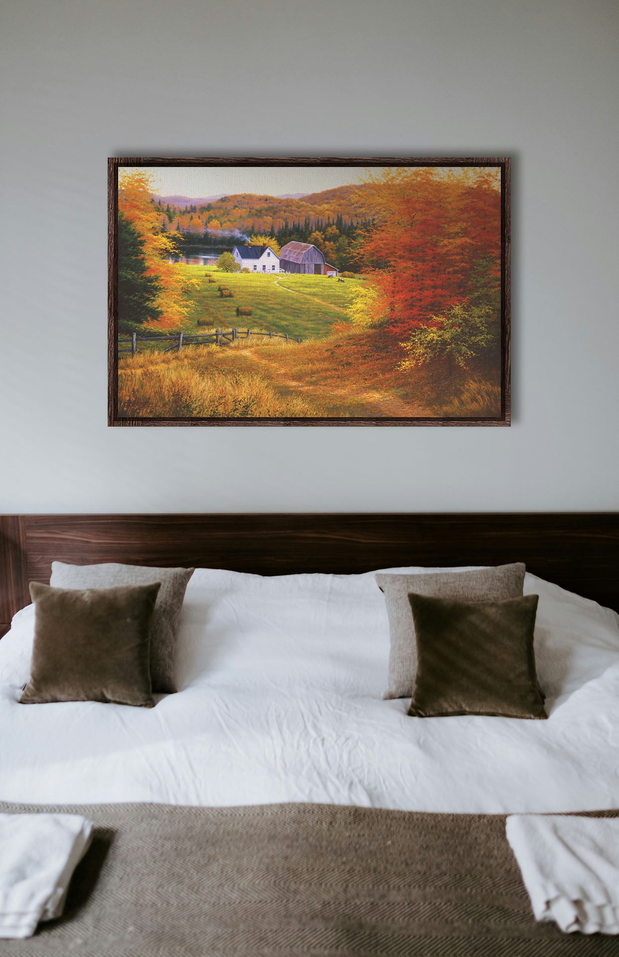 A painting hanging on a bedroom wall. A painting of a view looking down on a lakeside home and barn from a forest, featuring a few farm animals and hay bales. Printed on canvas in a float frame.