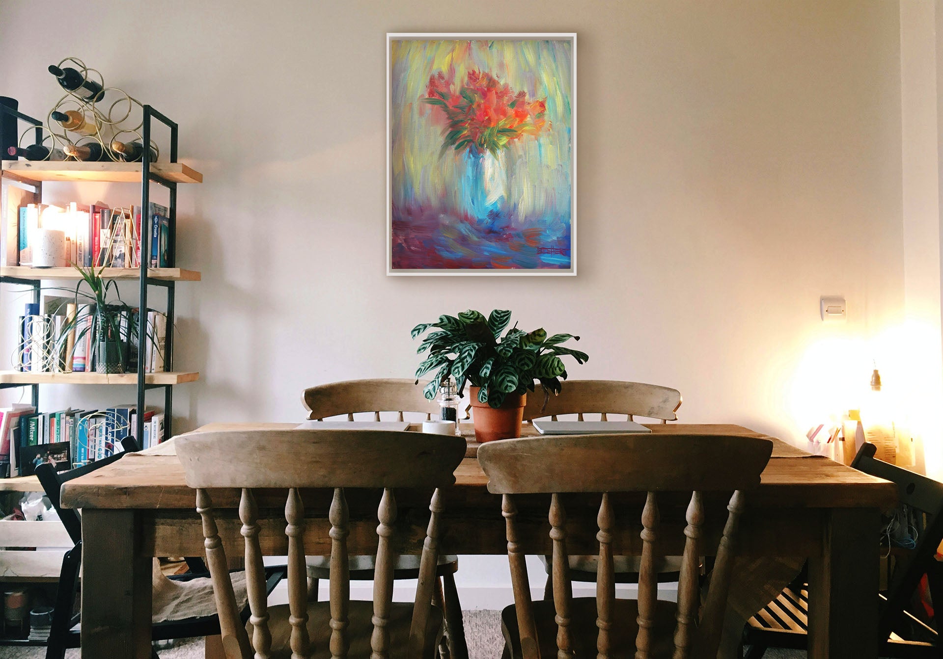 A painting hanging on a dining room wall. A still life painting of a vase of bright red flowers, created with expressive visible brushstrokes and broken color. Printed on canvas in a float frame.