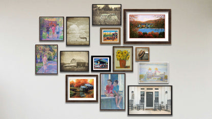 A collage of art in the luxury Window to the Past package, including five matted and framed paintings of a little town by the water, a vase of sunflowers, a family lost on their road trip, a family at a gas station, and an old mill; a framed photo of a hat on a chair; four float framed photos of a truck in a field, a farm house porch, and two barns; and four float framed paintings of kids on a window, people on a bench, a person walking their dog, and three kids walking.